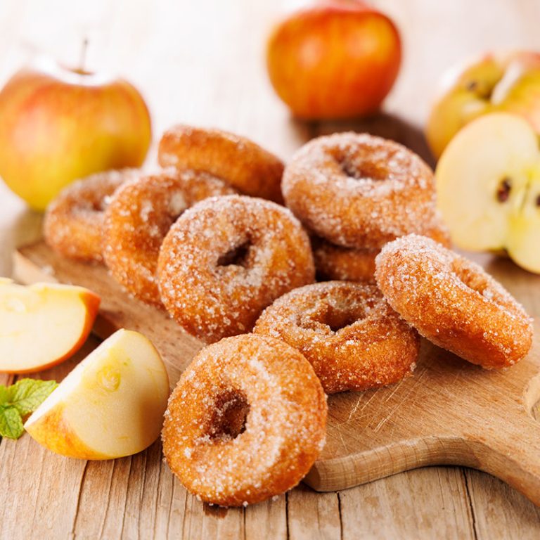 Apple cinnamon donuts dusted with sugar and surrounded by sliced apples